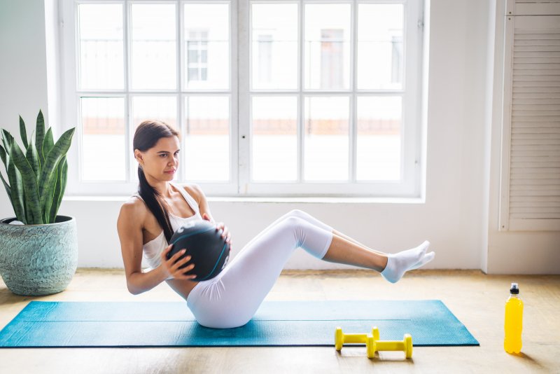 Young woman doing a medicine ball ab workout at home on a yoga mat next to window and potted plant (Photo by oneinchpunch - stock.adobe.com)